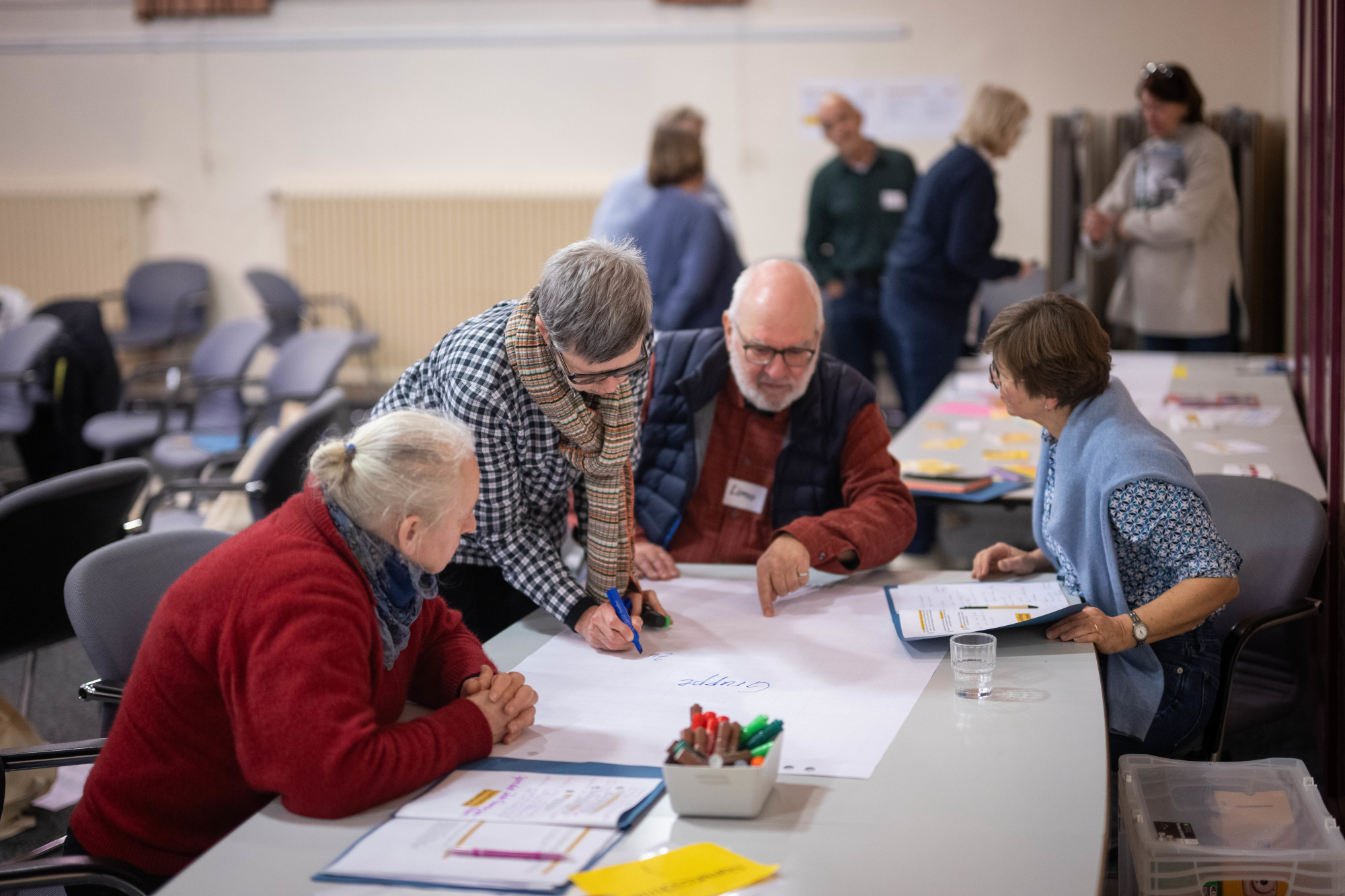 Foto von älteren Teilnehmenden am Workshop im FuturE-Programm. Sie sitzen und sind vertieft ihre Ideen gemeinsam auf ein großes Papier zu schreiben.