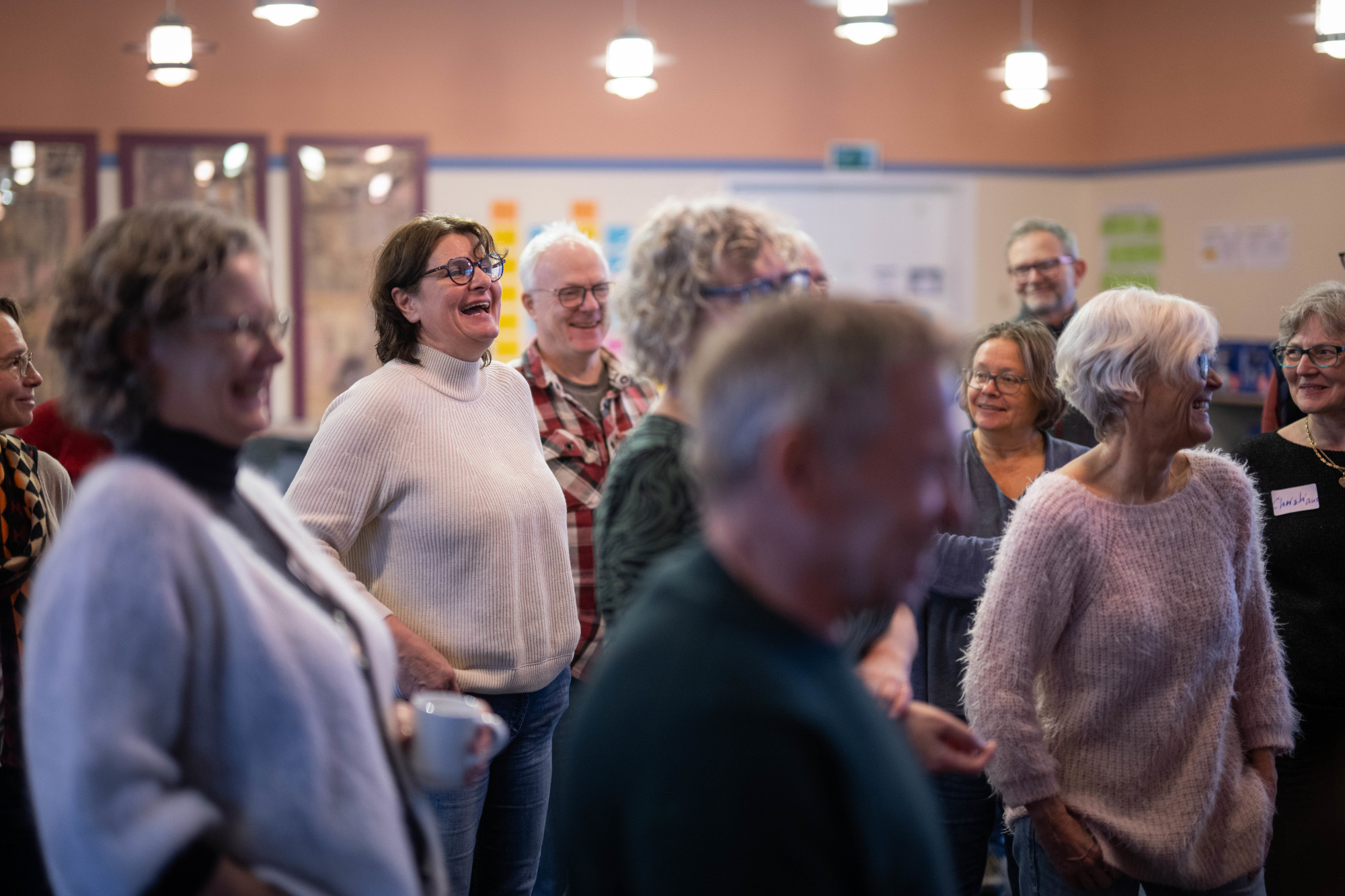 Neun Erwachsene, Frauen und Männer stehen und blicken in Richtung eines nicht sichtbaren Fokuspunktes. Sie lachen und haben offensichtlich Spaß bei dem, was sie gerade hörten.