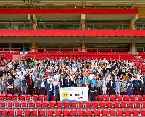 Gruppenbild auf einer Stadiontribüne mit den vielen engagierten Vertretern der Preisträger des Machen!2024 Wettbewerbs.