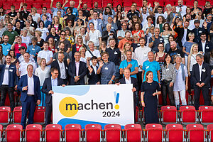 Gruppenbild auf einer Stadiontribüne mit den vielen engagierten Vertretern der Preisträgerinnen und Preisträger des Machen!2024 Wettbewerbs.