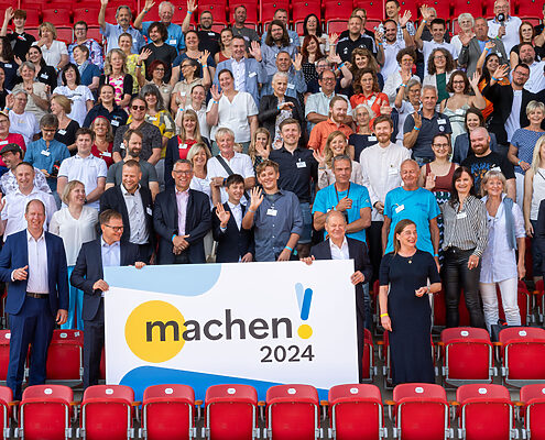 Gruppenbild auf einer Stadiontribüne mit den vielen engagierten Vertretern der Preisträgerinnen und Preisträger des Machen!2024 Wettbewerbs.